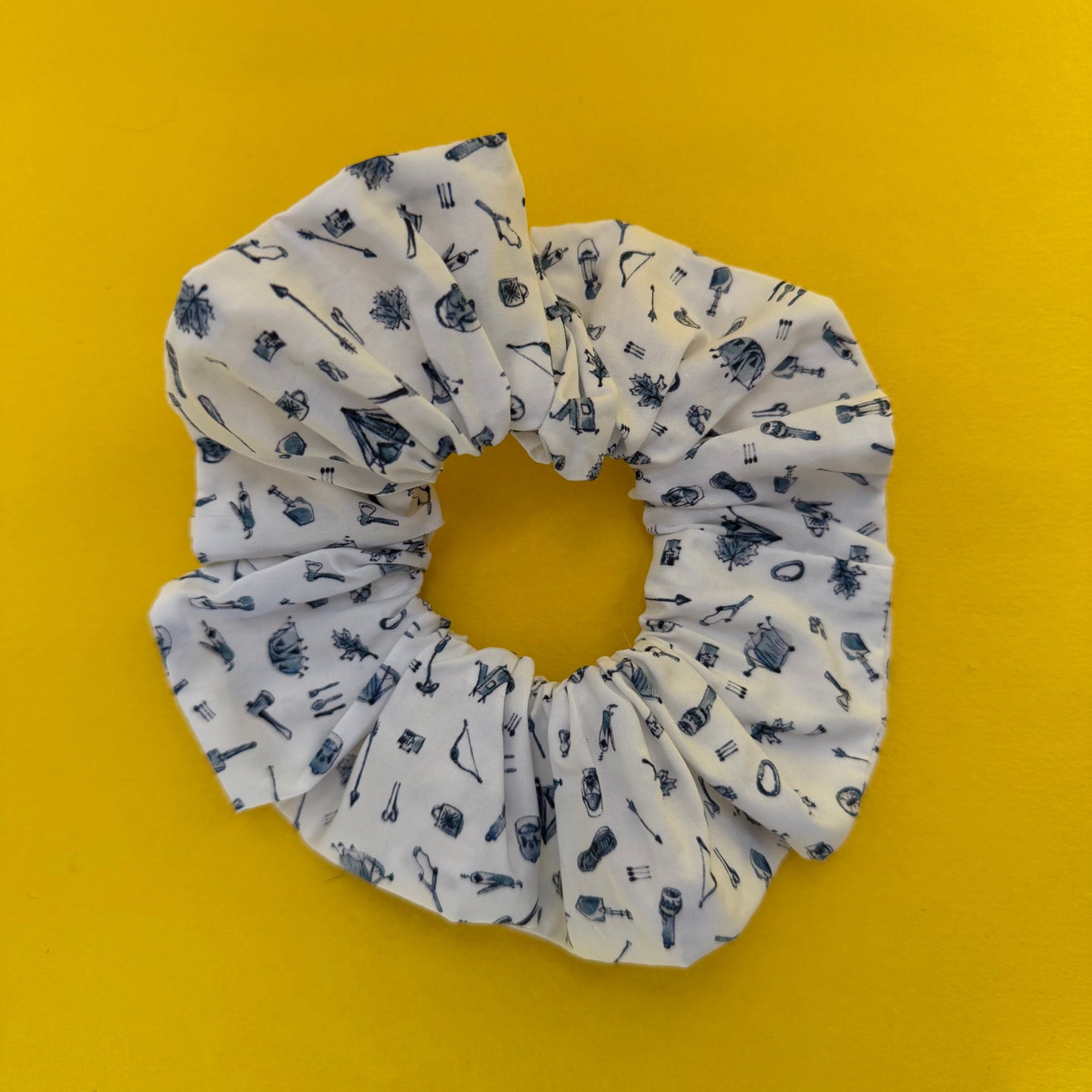 White scrunchie with blue camping icons pattern on a yellow background